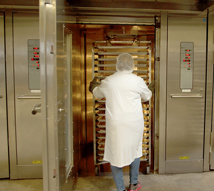 Bakery worker loading trays of cookies into an industrial oven
