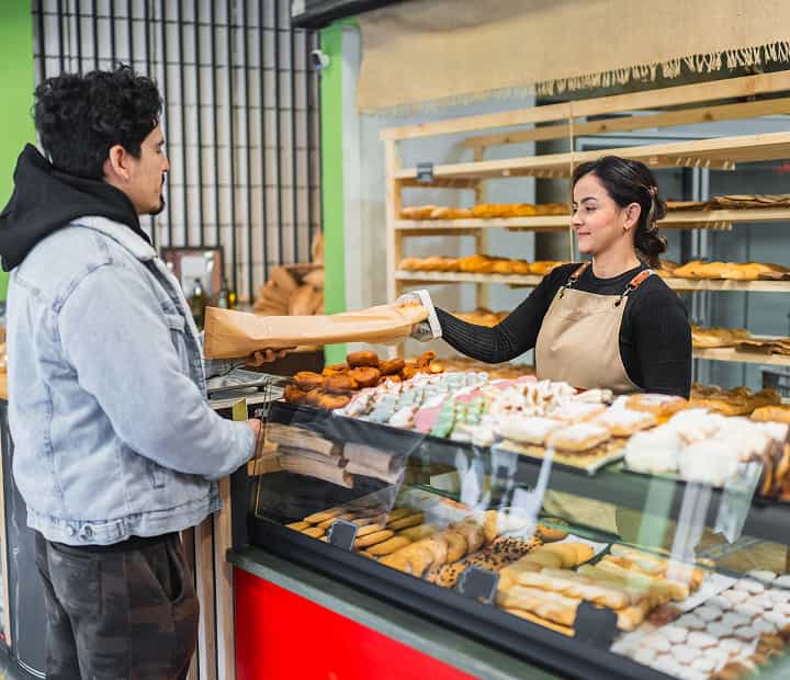 Bakery staff handing packaged cookies to a customer at an in-store bakery