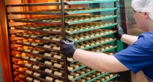 Bakery worker loading trays of cookies into a large industrial oven