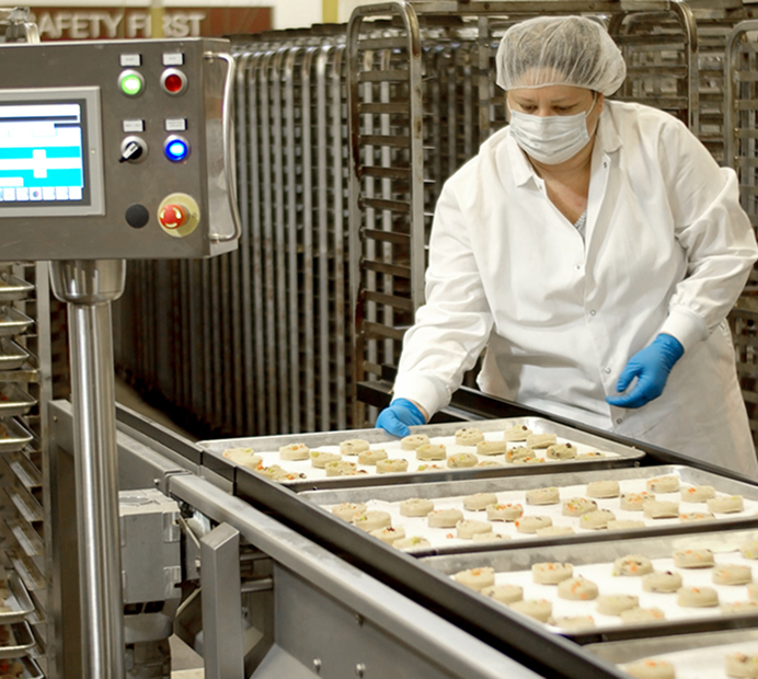 Bakery worker placing cookie dough portions onto trays on a production line
