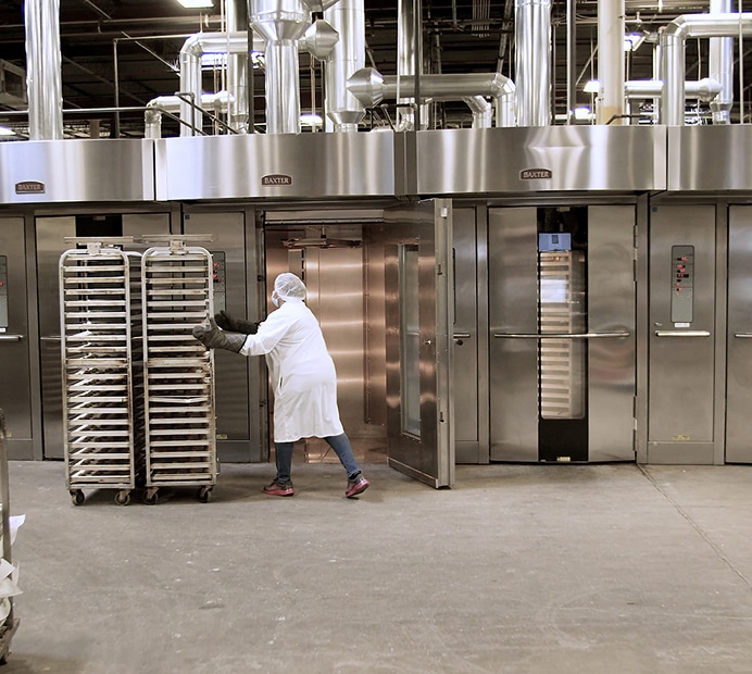 Bakery worker loading racks into large commercial ovens