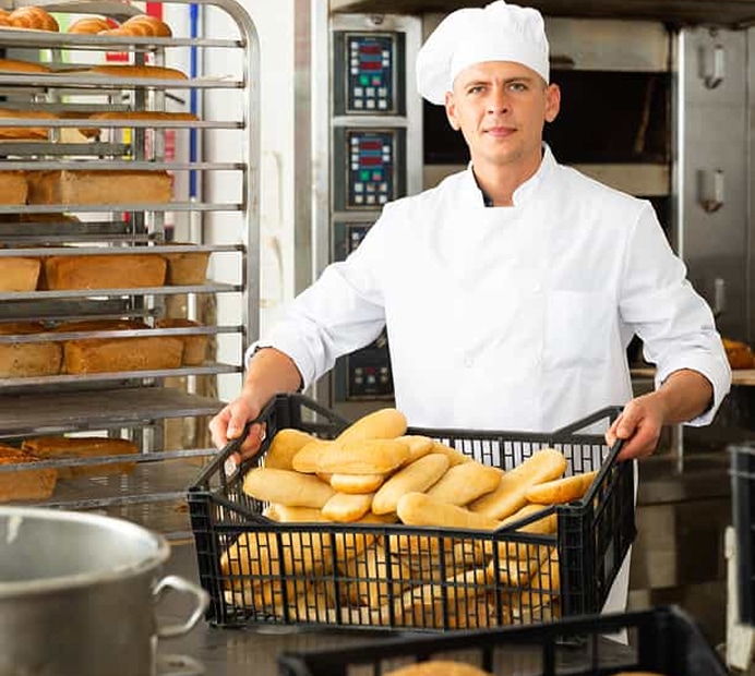 Baker holding a crate of freshly baked bread in a bakery manufacturing facility