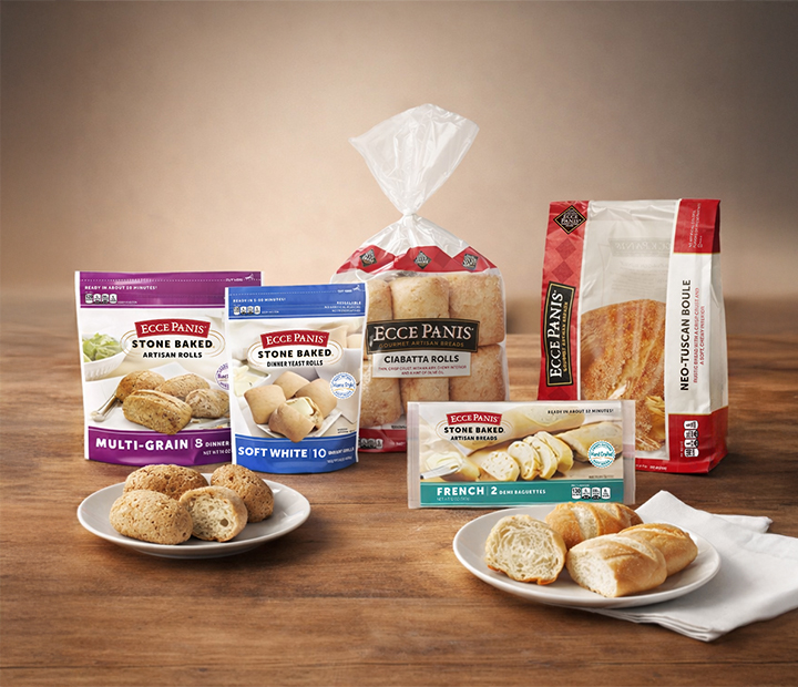 An assortment of Ecce Panis breads: multi-grain artisan rolls, soft white rolls, ciabatta rolls, and Tuscan boule, displayed on a wooden table
